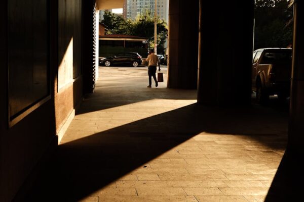 Juego de luces y sombras en arquitectura: impacto visual y funcionalidad Glimpse of a cityscape through an architectural passage with striking shadows.